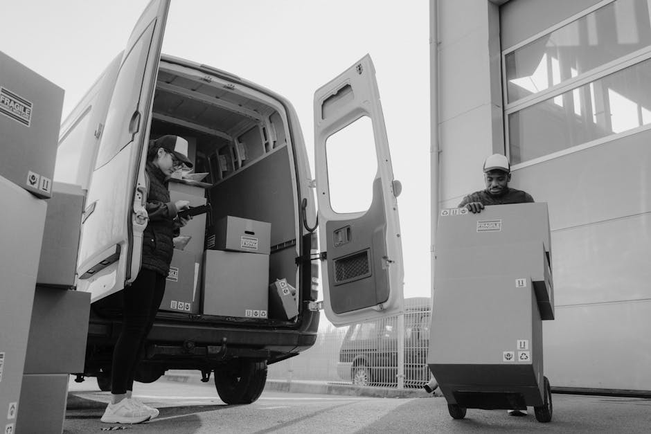 A professional house removals worker standing in front of a white moving van with the company logo 'MOVING COMPANY' and the tagline 'Local & Long Distance', parked on a street with a brick and stucco